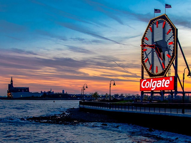malul mării, logo-ul Colgate în fundal, sub un ceas mare cu limbi roșii