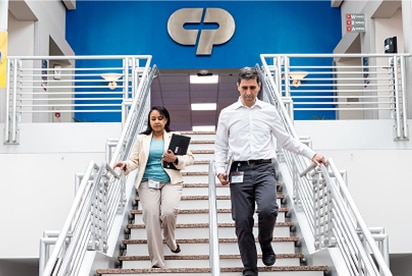 Angajații Colgate-Palmolive coboară o scară, având în spate logo-ul Colgate-Palmolive pe un perete albastru.
